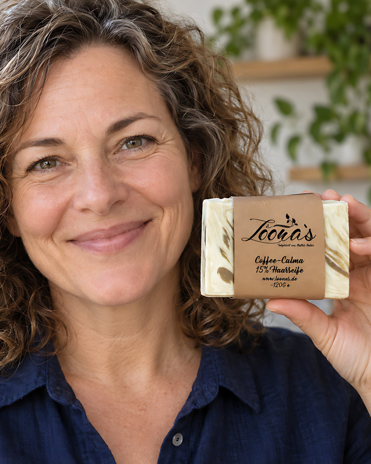 Nachher (Handy): lächelnde Frau um die 45 mit glänzenden Locken hält Loona's Coffee-Calma 15% Haarseife